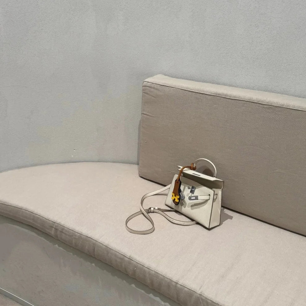 Charm sandale miniature accroché à un sac crème posé sur un banc