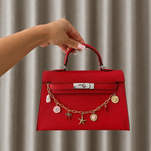 Chaîne dorée à charms drapée sur un sac rouge porté à la main